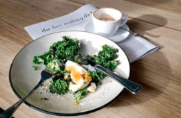 Kale and eggs breakfast on a plate with coffee and the sunday paper magazine