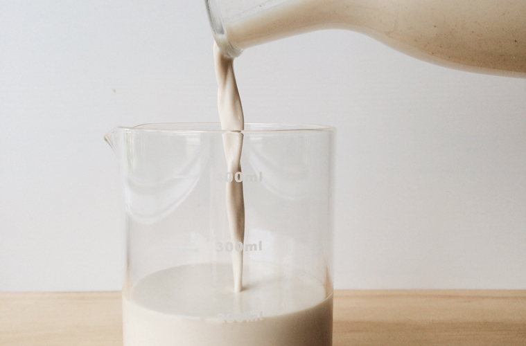 Nutmilk being poured fro a glass jug into a glass standing on a wooden surface