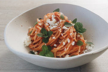 Roast Capsicum, Tomato and Garlic sauce with spaghetti, feta and mint in a white bowl