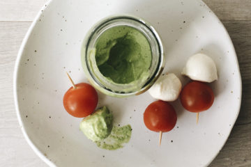 Tahini and Parsley Dressing in a glass jar with three cherry tomato and bocconcini sticks on a white plate