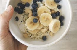 yoghurt, banana, blueberries, hemp seeds, sesame seeds in a white bowl