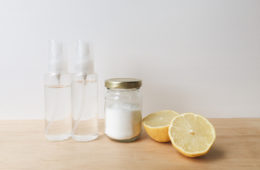 two clear spray bottles, citric acid in a glass jar, a lemon cut in two halves