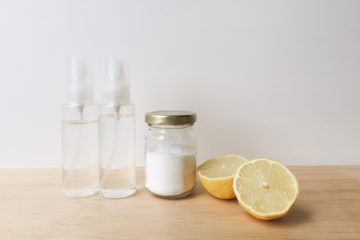 two clear spray bottles, citric acid in a glass jar, a lemon cut in two halves