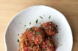 pork meatballs and spaghetti on a white plate with parmesan and parsley sprinkled over