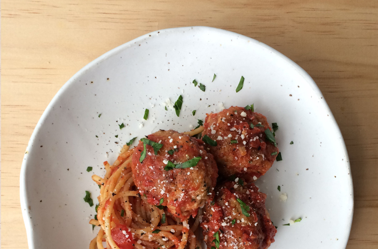 pork meatballs and spaghetti on a white plate with parmesan and parsley sprinkled over