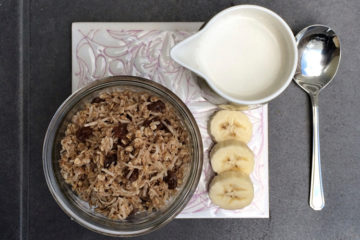 raw muesli in a glass jar with a jug of milk and slices of banana next to it