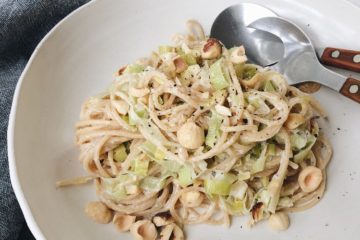 Vegan Pasta with leek and hazelnuts on a white plate with a grey napkin on the side