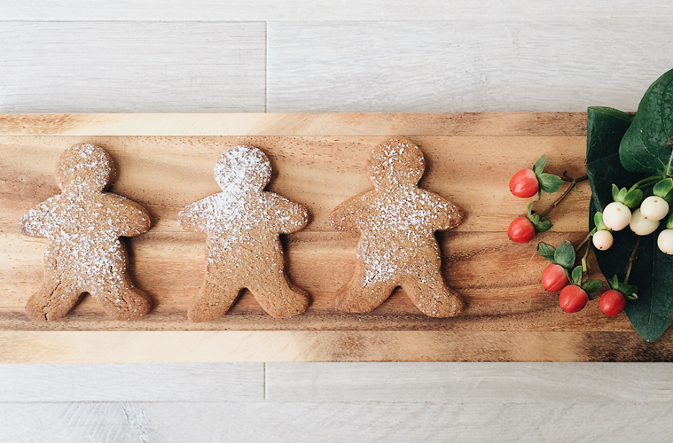 Buckwheat Gingerbread Men on a wooden board with some red and white flowers on the side