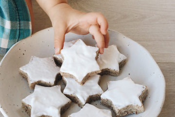 Cinnamon Stars on a white plate with a child's hand reaching for one and picking it up