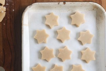 Muerbeteigplaetzchen cut out as stars on a baking tray pre-baking, with some leftover dough next to it on the left hand side