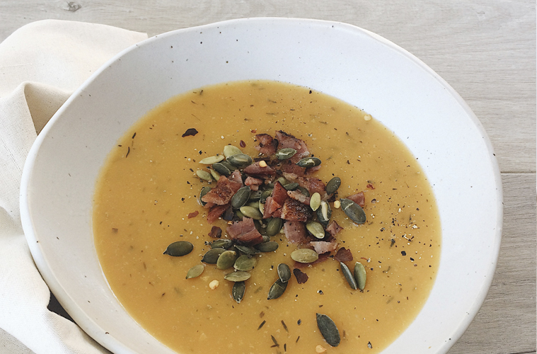 Pumpkin soup in a white bowl sprinkled with bacon and pumpkin seeds