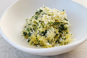 baked spaghetti squash with parsley and parmesan in a white bowl on a wooden surface
