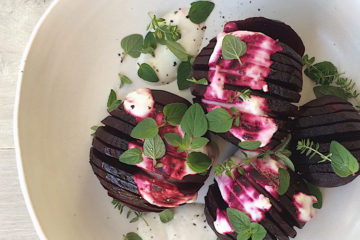 Hasselback Beets with yoghurt dressing and fresh oregano on a white plate