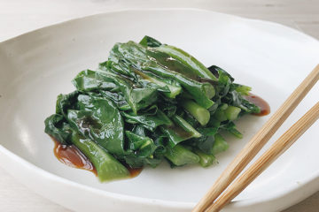 asian greens on a white plate with chopsticks on the side