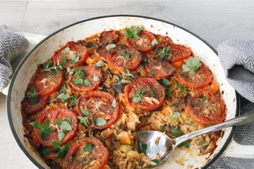 baked orzo in a shallow pan topped with tomato slices and fresh oregano
