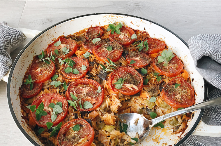 baked orzo in a shallow pan topped with tomato slices and fresh oregano
