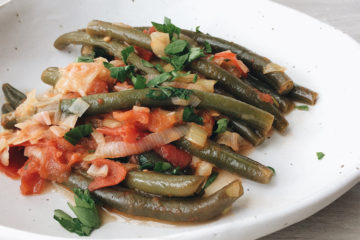 braised green beans with tomato and onion on a white plate