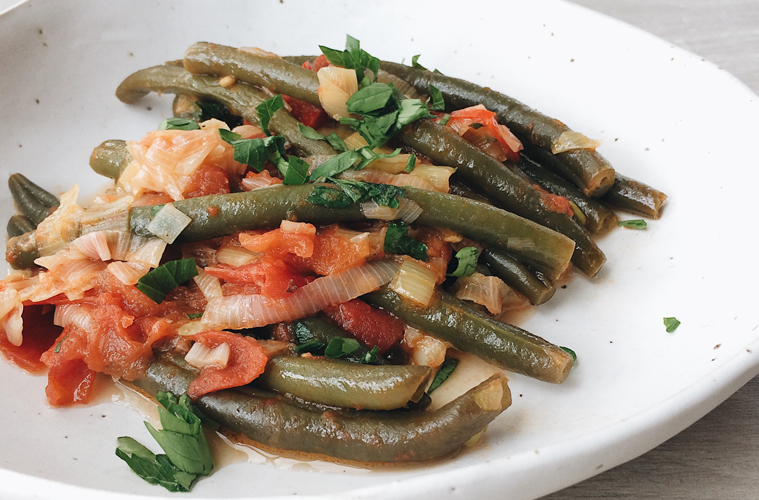 braised green beans with tomato and onion on a white plate