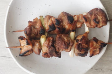chicken yakitori skewers on a white plate on a wooden surface