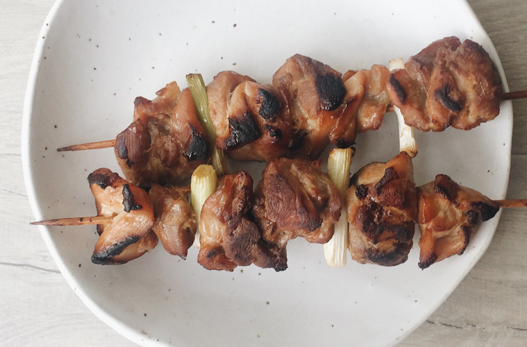 chicken yakitori skewers on a white plate on a wooden surface