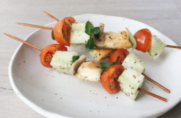 greek salad skewers on a white plate on a wooden surface