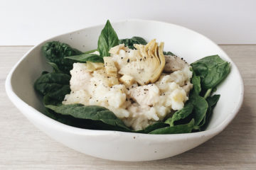 oven baked chicken risotto on baby spinach leaves in a white bowl on a wooden surface