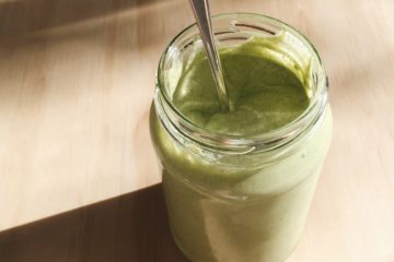 spicy green tahini dressing in a glass jar on a wooden surface