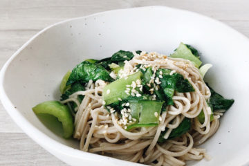 Soba noodles and bok choy with miso in a white bowl on a wooden surface