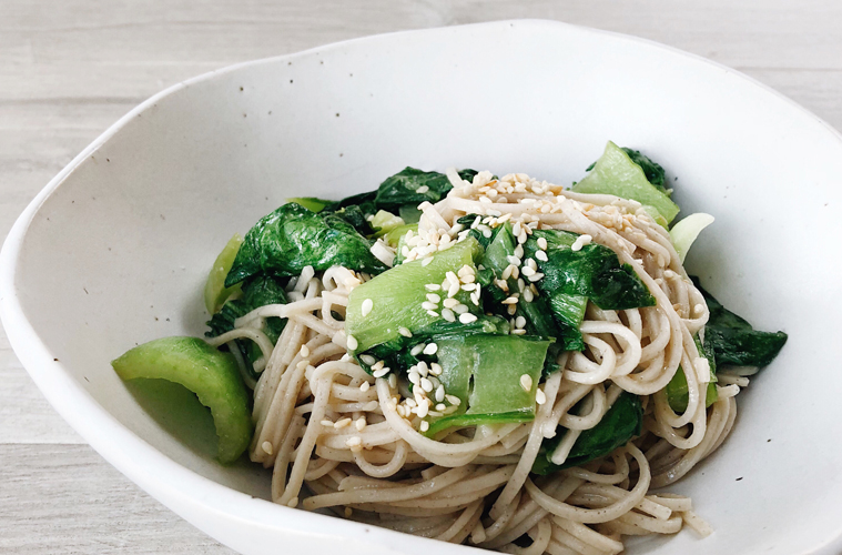 Soba noodles and bok choy with miso in a white bowl on a wooden surface