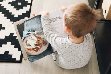 Little boy reading cookbook sitting on the floor with his back to the camera