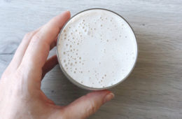 Banana, oat and honey smoothie in a glass on a wooden surface held by a hand
