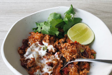 Chilli con carne in a white bowl with a spoon, lime and fresh coriander