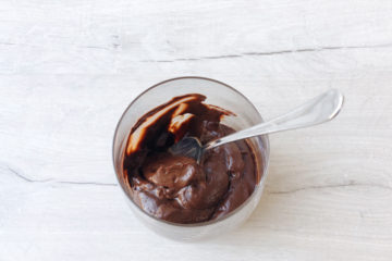 avocado chocolate mousse in a glass with a spoon on a wooden surface