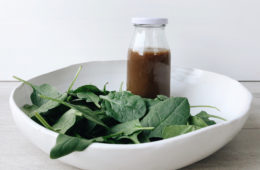 honey, orange and balsamico dressing in a jar in a white bowl with baby spinach leaves