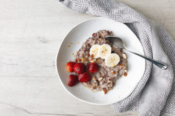 vegan breakfast rice porridge with strawberries and banana on a white plate