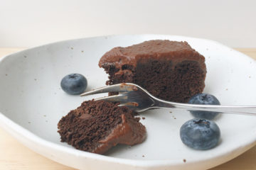 vegan chocolate cake on a white plate with blueberries and a fork
