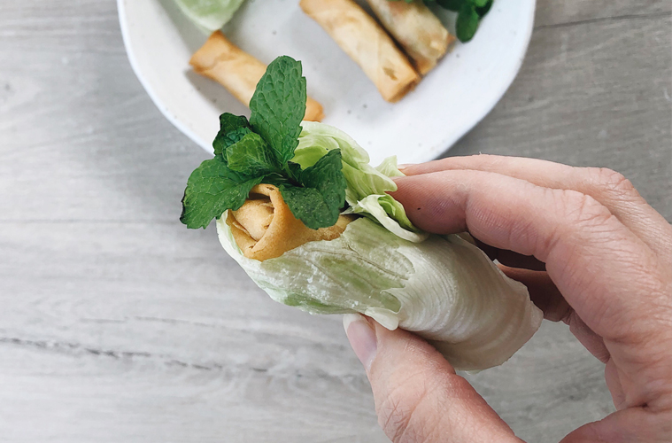 a springroll wrapped in lettuce and mint held in a hand